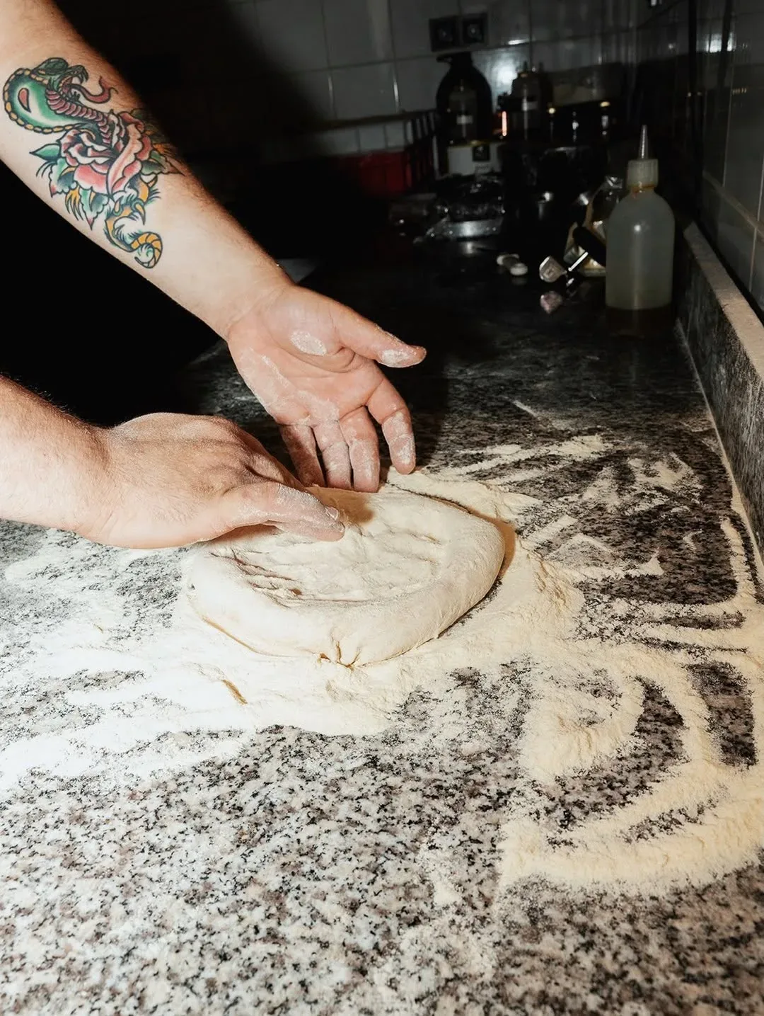 Hands stretching pizza dough on a floured marble counter at Knack & Snack